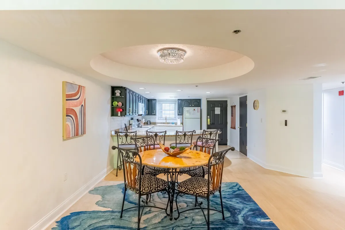 A cozy and stylish dining nook featuring a round table, decorative chandelier, colorful wall art, and a view into the kitchen area. The setting is ideal for both intimate family dinners and lively celebrations.