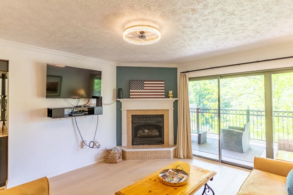 A cozy living room with a stone fireplace, a large TV, inviting sofa, and expansive windows that welcome natural light. The space is arranged for family gatherings, storytelling, or relaxing evenings after outdoor adventures.