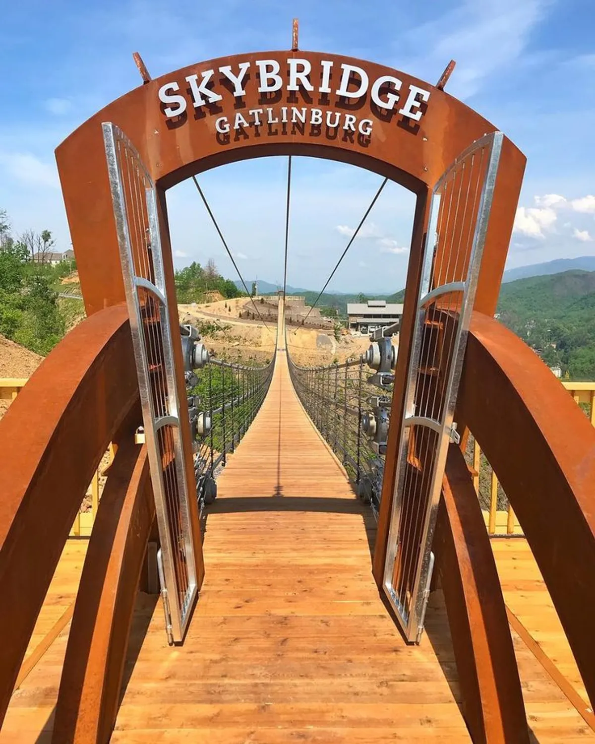 A dramatic entrance to the SkyBridge stretches across a wooden walkway with panoramic mountain views in the distance. The scene is lively and inviting, highlighting the thrill of exploration and the unique outdoor experiences available nearby.