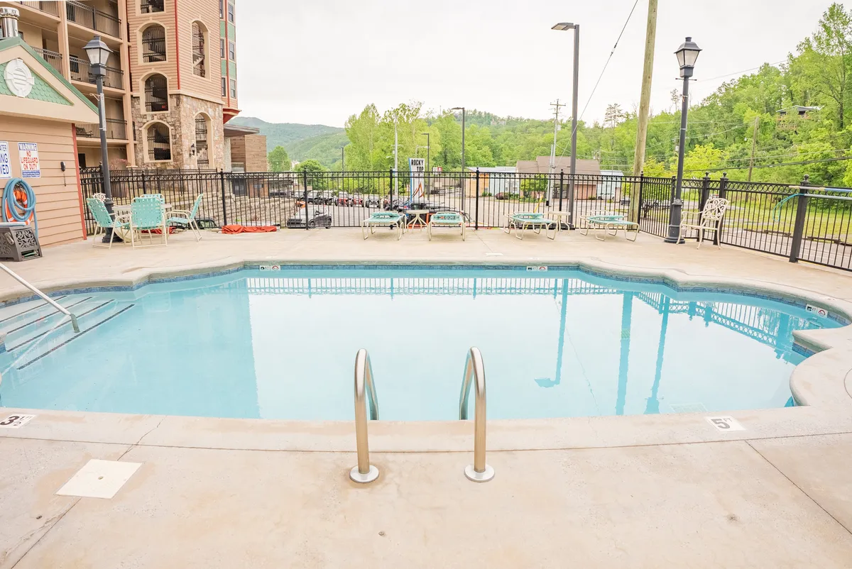 A serene exterior view of the sparkling swimming pool surrounded by lush greenery. Lounge chairs are positioned poolside, inviting guests to sunbathe, socialize, or simply relax by the water. The tranquil ambiance suggests a perfect spot for both sunrise swims and relaxing sunset moments.