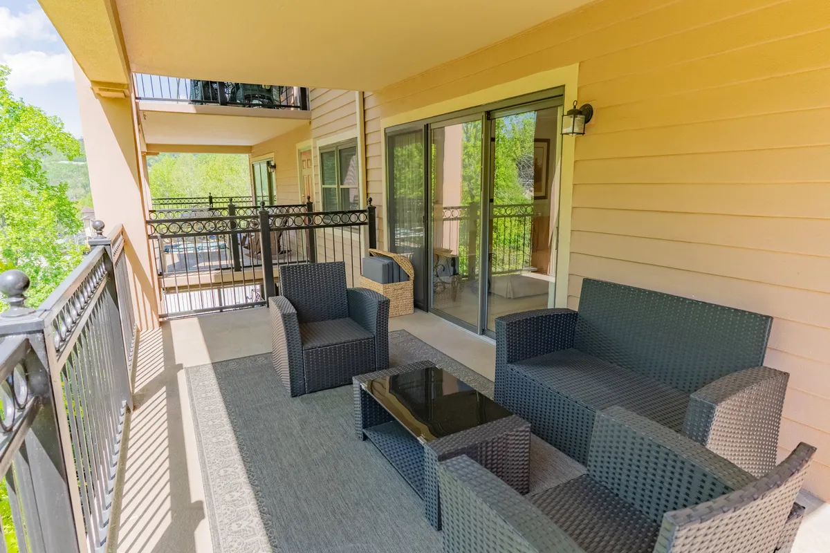 This image features a balcony with woven lounge chairs and a glass coffee table looking out over a tranquil setting. The arrangement is perfect for small gatherings, coffee in the morning, or relaxing after a night out.