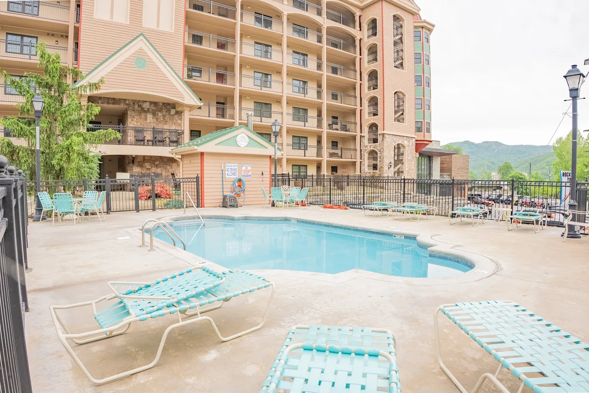 A tranquil resort pool area surrounded by lounge chairs and lush greenery. The pool is positioned to take advantage of stunning mountain views in the background, creating the perfect spot for relaxation or a romantic moment at sunset.