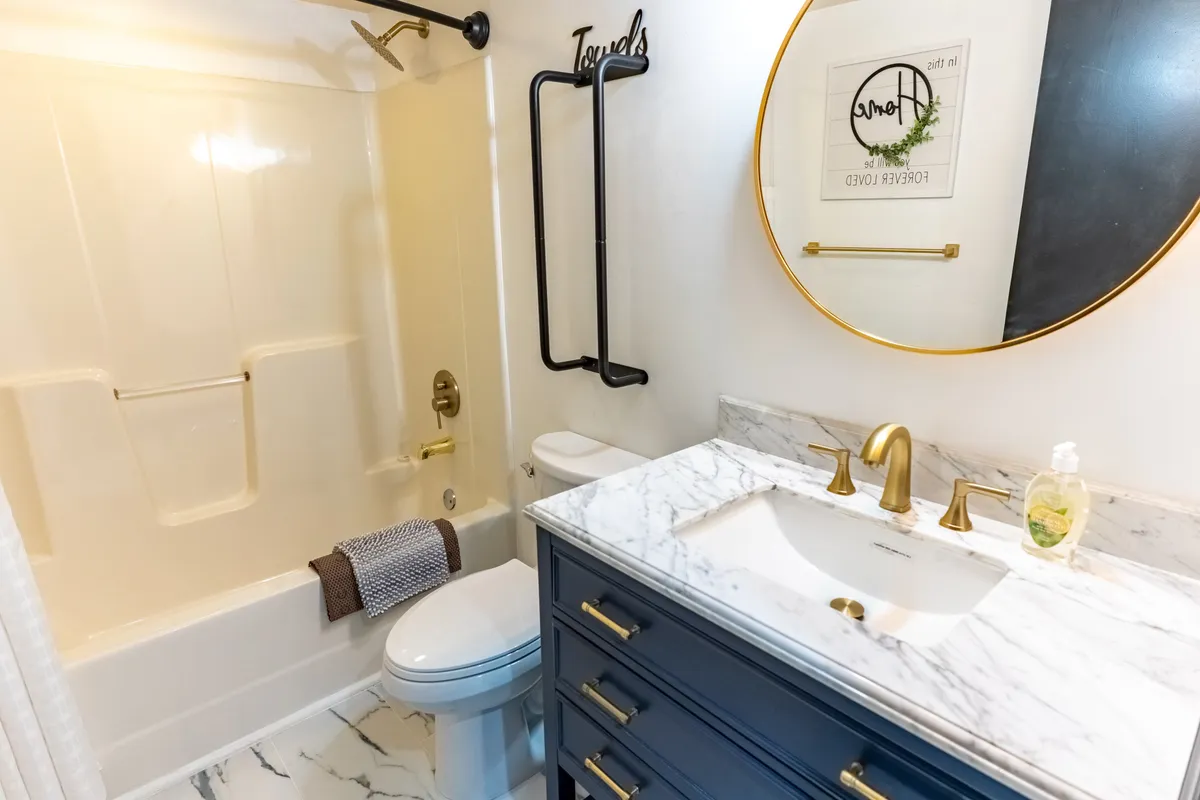 An elegant bathroom scene with a marble countertop, gold fixtures, a round mirror, and a dark blue vanity. The space is inviting and sophisticated, evoking a spa-like atmosphere for refreshing and unwinding.