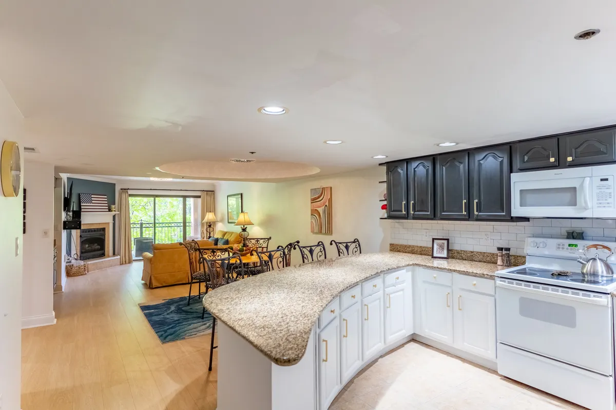 A spacious, open-concept living area that seamlessly connects the kitchen and living room. The focal point is a cozy fireplace, surrounded by plush, comfortable seating. The area is bright and welcoming, perfect for both family gatherings and intimate evenings. The kitchen island sits just adjacent to the living area, encouraging easy conversation and participation in activities across both spaces.
