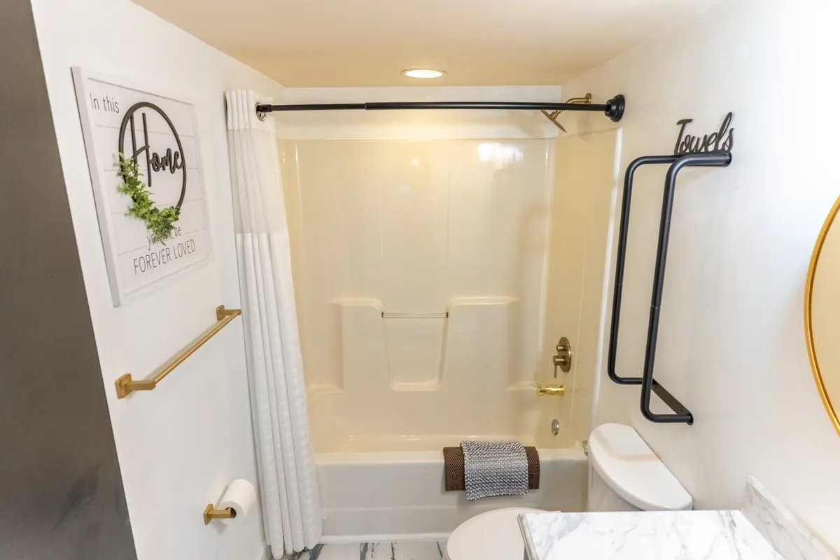A stylish bathroom featuring a bathtub, a well-lit mirror, a towel rack, and a decorative wall sign. The space feels calm and welcoming, ideal for a peaceful soak or getting ready for the day.